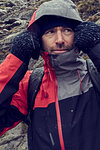 Male hiker pulling hood up in sleeting rugged landscape, close up, Llanberis, Gwynedd, Wales