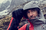 Male hiker pulling hood up in sleeting snow capped mountain landscape, close up, Llanberis, Gwynedd, Wales