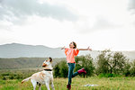 Girl with open arms playing with labrador dog in scenic field landscape, Citta della Pieve, Umbria, Italy