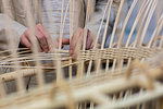 Young female basket maker weaving in workshop, mid section