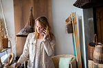 Young female basket maker making smartphone call in workshop