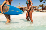 Young women in bikinis with surfboard in sunny ocean