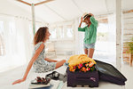 Young women friends unpacking suitcase in beach hut bedroom