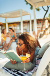 Carefree woman relaxing, reading book and drinking cocktail on beach patio