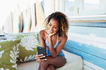 Happy young woman using smart phone on beach hut patio