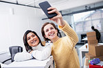 Smiling businesswomen taking selfie in new office