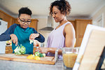 Mother and son cooking, cutting vegetables in kitchen