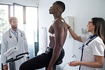 Doctor watching nurse perform ECG test on patient in consultation room