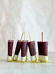 Tri-coloured ice lollies in a row on table, white background