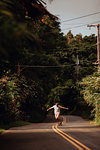 Mid adult male skateboarder skateboarding on centreline along rural road, Haiku, Hawaii, USA