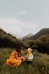 Mother looking at wildflower with toddler daughter in rural valley, Mineral King, California, USA