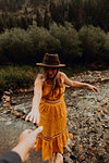Pregnant woman in orange maxi dress reaching for hand from rural river, Mineral King, California, USA