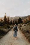 Young woman in maxi dress wearing backpack walking along rural road, rear view, Mineral King, California, USA