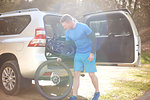 Male cyclist removing bike tire from back of SUV in sunny parking lot