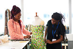 Female fashion designers pinning dress on dressmakers model in studio