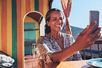 Smiling, happy woman taking selfie with smart phone on sunny patio