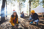 Portrait smiling girl gathering kindling at sunny campsite in woods