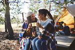 Happy lesbian couple relaxing, drinking coffee at sunny campsite