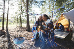 Happy lesbian couple relaxing, drinking coffee at sunny campsite in woods