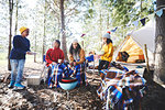 Lesbian couple and kids cooking at campsite grill in sunny woods