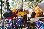 Happy, affectionate lesbian couple and kids hugging at campsite