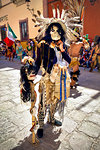 Indigenous tribal dancer in a skeleton mask and holding a skull with hair at a St Michael Archangel Festival parade in San Miguel de Allende, Mexico