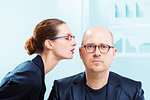 Mobbing concept of businesswoman whispering into man ear at workplace