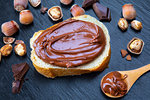 Slice of bread with spread chocolate cream and hazelnuts on black table. Serving a delicious breakfast concept.