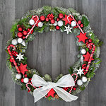 Christmas and winter wreath with candy canes, bow, bauble decorations, holly, mistletoe, ivy and spruce fir on rustic grey wood  background.