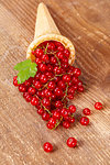 Red currant fruits in ice cream cone on wooden table. Focus on redcurrant.