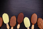 Ice cream on stick covered with chocolate on black stone slate board.