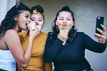 Young woman and teenage sisters posing for selfie while eating cakes