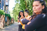 Young woman with teenage sisters looking at smartphone by park