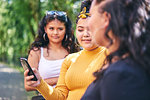 Young woman with teenage sisters looking at smartphone by park, over shoulder view