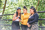 Young woman with teenage sisters looking at smartphone in park