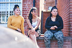 Young woman and her teenage sisters sitting on wall looking away