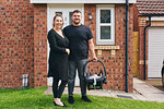 Couple carrying baby in cradle in front of house