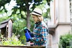 Mid adult woman spraying plants in her garden, side view