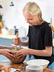 Girl and her sister baking a cake, stirring cake mixture in mixing bowl at kitchen table