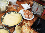 Messy baking preparation on kitchen table with cake mixture, kitchen scales, kitchen utensils and digital tablet