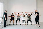 Fitness instructors observing friends doing squat against wall with resistance band in studio