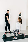 Fitness instructor observing woman doing lunges with kettlebell in studio
