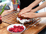 Girl and her sister baking a cake, pressing down top layer at kitchen table, cropped view of hands