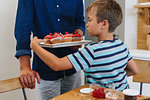 Father serving tray of cupcakes to boy at home