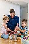 Father and children decorating cupcakes with frosting in kitchen
