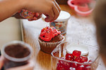 Hand dropping coloured sprinkles onto cupcake