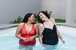 Two mid adult women standing in outdoor swimming pool laughing together, Cape Town, South Africa