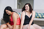 Two mid adult women sitting on outdoor poolside laughing together, Cape Town, South Africa