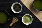 Still life of matcha tea preparation with whisk and bowls of matcha tea and tea powder, overhead view