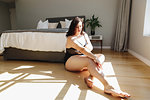 Woman applying body lotion in bedroom